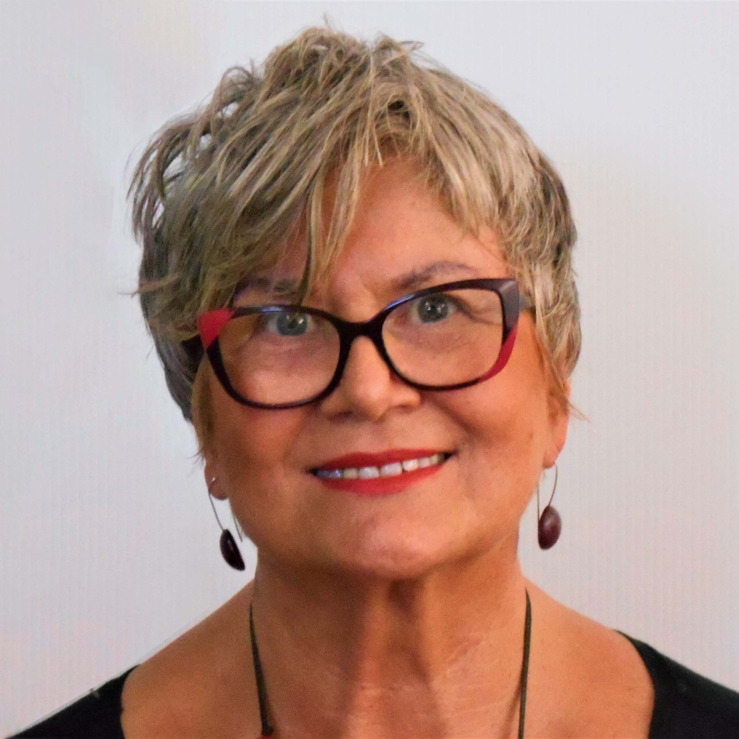 Profile photo of a Elizabeth Szczepanska, lights skin female, 60's, red and black frame glasses and earrings